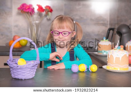 Cute little girls with down syndrome at home in the kitchen with Easter colored eggs and cakes.