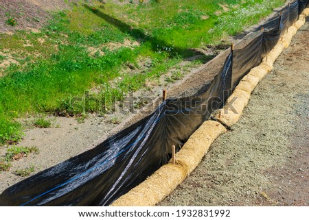 Straw wattles and plastic fence placed along dry waterway to reduce soil erosion, debris runoff and retain sediment during construction and maintenance project. Royalty-Free Stock Photo #1932831992