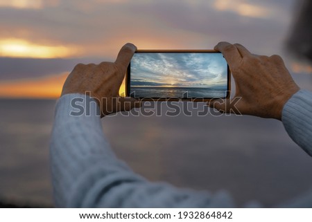 Close-up of woman hands photographing seascape at sunset with mobile phone