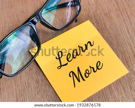 Phrase LEARN MORE written on sticky note with eye glasses.