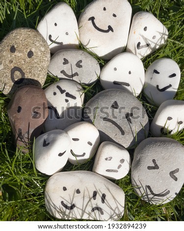 Emotion management concept, stones with painted faces symbolize different emotions. We are all different, but all together, learning to manage emotions.Against the background of green young grass