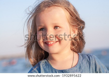 Little cute girl in a blue dress at the sea, the child smiles, childrens tourism and recreation on the beach.
