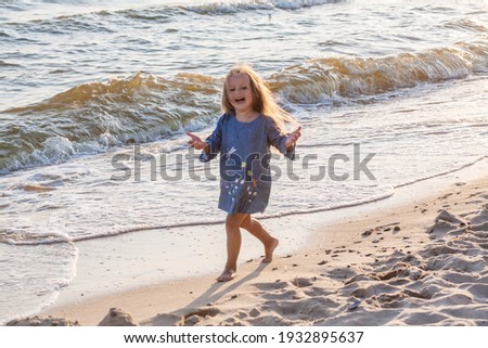 Little cute girl in a blue dress at the sea, the child smiles, childrens tourism and recreation on the beach.
