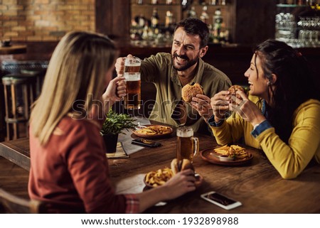 Young happy man toasting with friends while having lunch in a pub.
