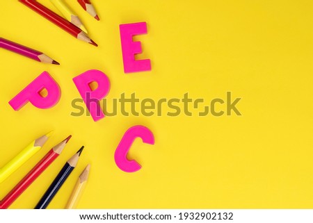 On the left on a yellow background pink plastic letters and colored pencils. A template with a workspace. Education
