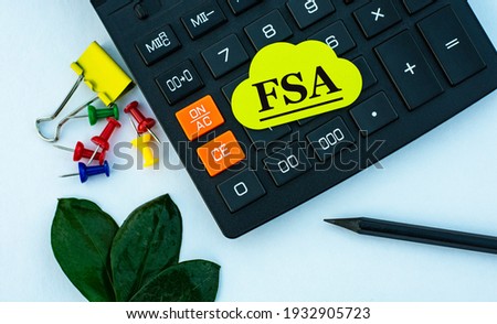 FSA (Flexible Spending Account) - acronym on yellow note paper on the calculator. On a white background are stationery clips with a pencil. Business and finance concept