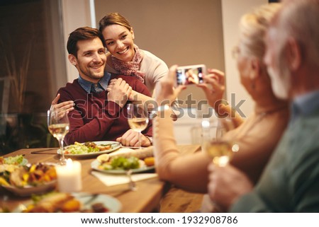 Happy family taking pictures with smart phone during a dinner at dining table. Focus is on young couple. 