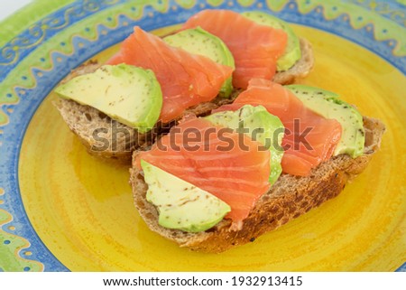 Homemade toast sandwich with salmon and avocado on a slice of cereal bread. The toast lies on a bright yellow plate. healthy food.