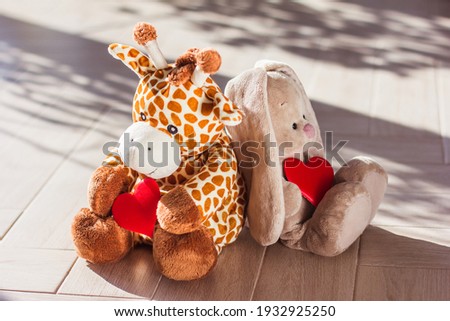Children's soft plush toy giraffe and bunny sit on wooden background, hard light and shadow