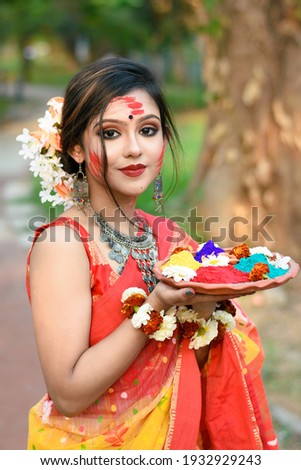 Portrait of pretty young indian girl wearing traditional saree and jewellery, holding powder colours in plate on the festival of colours called Holi, a popular hindu festival celebrated across India. Royalty-Free Stock Photo #1932929243