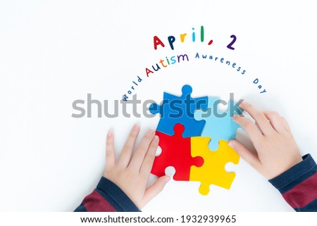 "World autism awareness day - April 2" Top view - hands of a young autistic boy playing with colorful puzzles pieces on white table. Kids mental health concept. Autism Spectrum Disorder, Supportive.