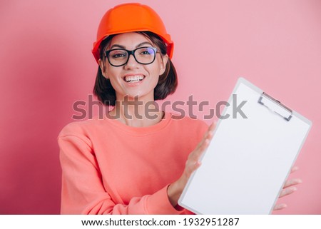 Smiling woman worker builder hold white sign board blank against pink background. Building helmet.