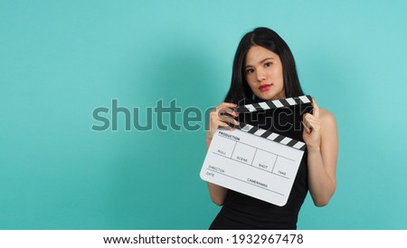 clapper board or movie clapperboard in teenage girl or woman hand with black and yellow color.it use in video production ,film, cinema industry on green or Tiffany Blue background.she wear black dress