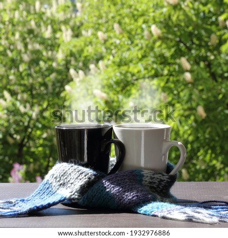 black and white coffee cups wrapped in a scarf against the backdrop of a view from the window of blooming trees. so different but together