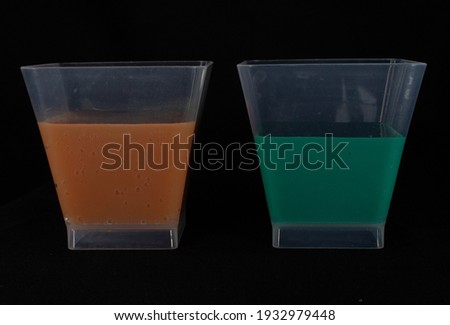 close up of two plastic cups half full of green and orange liquid isolated on a black background