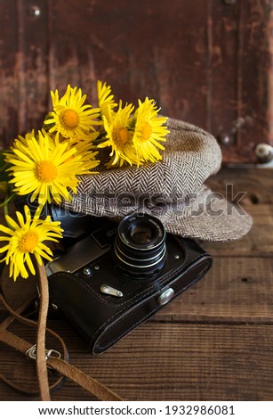Close-up of an old camera with a vintage hat and a bouquet of yellow flowers on a wooden background.