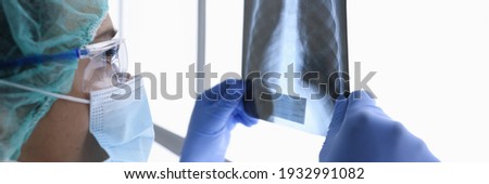 Woman doctor in protective medical mask and glasses looks at an X-ray picture. Medical examination of internal organs concept