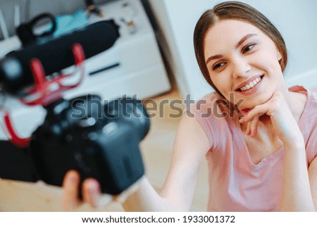 Attractive young blogger holding a camera with microphone and touching her chin while smiling Royalty-Free Stock Photo #1933001372
