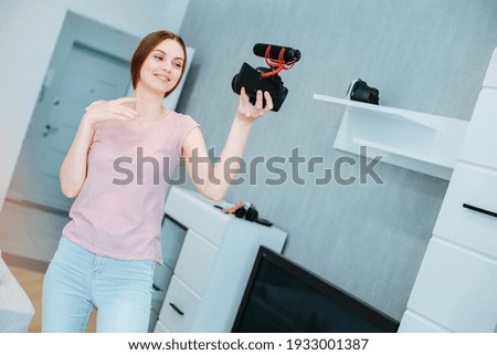 Happy young lady in casual clothes standing with a camera and microphone and smiling Royalty-Free Stock Photo #1933001387