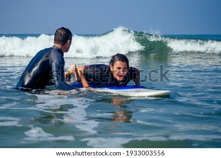 man instructor demonstrating how to paddle in the water by hands on surfboard to indian woman in surf class in Goa sea Royalty-Free Stock Photo #1933003556