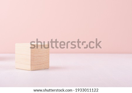 Beige natural wood podium of cube shape on white wood table and pastel pink wall. Showcase for cosmetic products, packings.