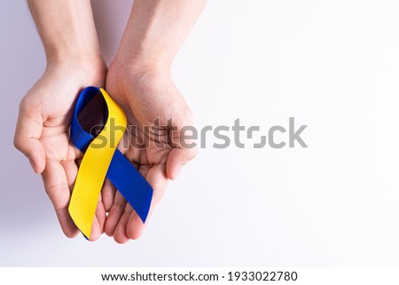 Down syndrome day, hands holding blue yellow ribbon awareness support patient with illness disability