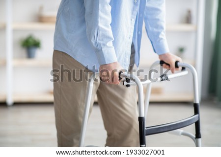 Cropped view of elderly man walking with frame at home, closeup. Unrecognizable senior male using medical equipment to move around his house. Disabled older person in need of professional help Royalty-Free Stock Photo #1933027001