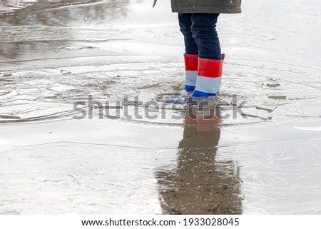 Low angle of a dutch girl wearing a boots in colour of Netherlands flag (white, red, blue) Young women standing in frozen lake with cracked ice with reflection, Outdoor winter activity for children.