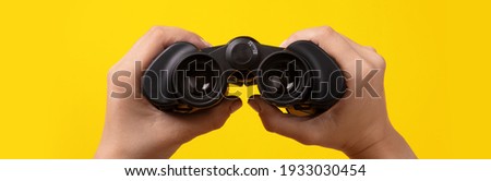 binoculars in hand over yellow background, find and search concept Royalty-Free Stock Photo #1933030454