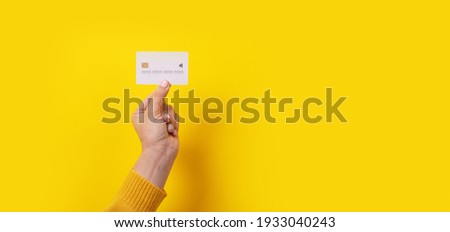 white credit card in hand over yellow background, panoramic image