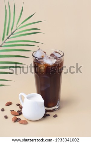 cold iced black coffee with almond milk in a jug on a beige background, summer drink, vertical Royalty-Free Stock Photo #1933041002