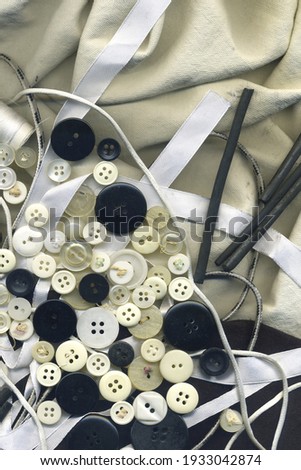 Buttons, white silk, thread black and white image. Collection of assorted spare clothes buttons with textile tools vintage. Needlework buttons frame on fabric texture wallpaper