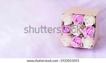 Banner with bouquet white and purple roses in pink paper box above violet background. Close up copy space image in pastel colors