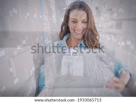 Composition of smiling woman using laptop over stack of cardboard boxes in warehouse. moving house, global shipment and delivery concept digitally generated image.