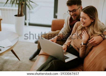 Handsome young couple using laptop together while sitting on sofa at home Royalty-Free Stock Photo #1933067657