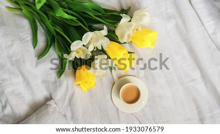 Breakfast in bed. A bouquet of tulips lies on the bed next to a cup of hot coffee. Spring. Gift. Good morning. White and yellow flowers.