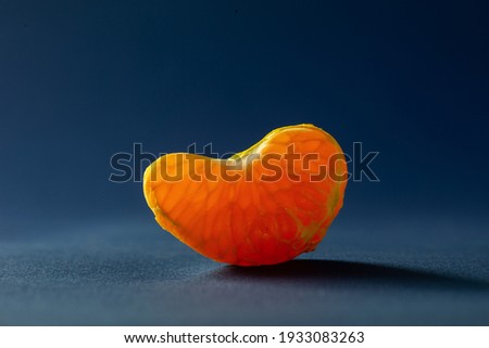 Juicy mandarin slice macro photography. A piece of bright orange tangerine close-up on a dark blue background.