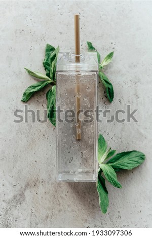 Top view of glass container with clean water and straw placed near mint leaves on gray stone surface