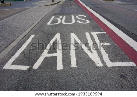 White letters on road "Bus Lane" with  rad and white lines on the asphalt road to limit vehicles can't use it except public bus