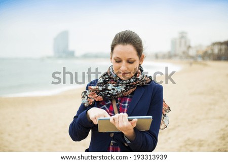 Portrait of pretty young traveler with digital tablet on the beach on a cold day.