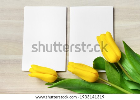 mock up of three yellow tulips and two paper blocks lie on a wooden surface