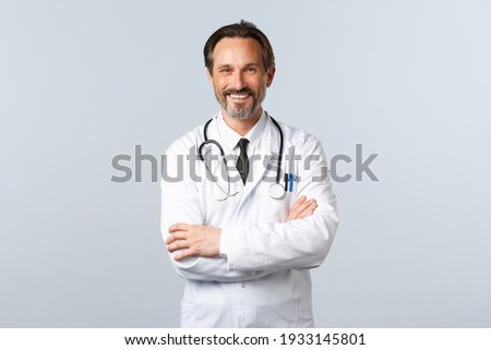 Covid-19, coronavirus outbreak, healthcare workers and pandemic concept. Enthusiastic smiling doctor, physician in white coat looking enthusiastic, cross arms chest, listening to patient Royalty-Free Stock Photo #1933145801