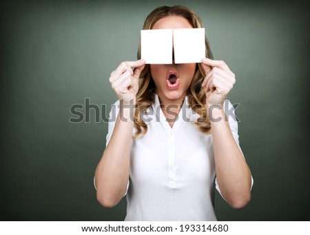 Portrait of young cute girl holding two blank card on her eyes isolated on grey background, surprised facial expression, advertisement concept