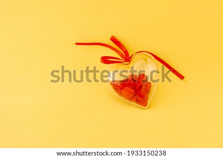 Transparent gift box in the form of a heart with lots of little red hearts inside on a yellow background. view from above. Top view. flat lay. Copy space. concept Valentines day and for love stories