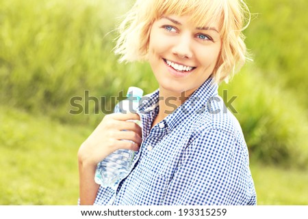 A picture of a happy relaxed woman standing with a bottle of water over green background