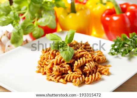 A picture of Italian pasta with red pepper pesto served on a white plate and decorated with basil