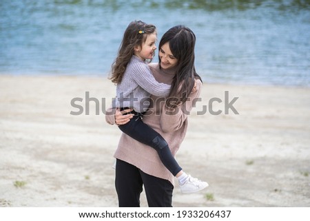 Happy woman and little girl playing together outside on scenic spring sandy beach. Mother hugging her little daughter. Happy white family of young mom and daughter enjoying warm spring nature outside