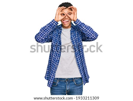 Young handsome african american man wearing casual clothes doing ok gesture like binoculars sticking tongue out, eyes looking through fingers. crazy expression. 