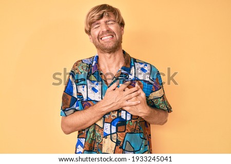 Young blond man wearing summer shirt smiling with hands on chest with closed eyes and grateful gesture on face. health concept. 
