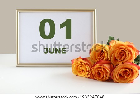 day of the month 01 June calendar photo frame and yellow rose on a white table.